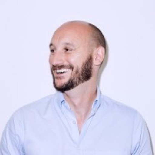 Smiling man with a beard wearing a light blue button-down shirt, looking to his left.