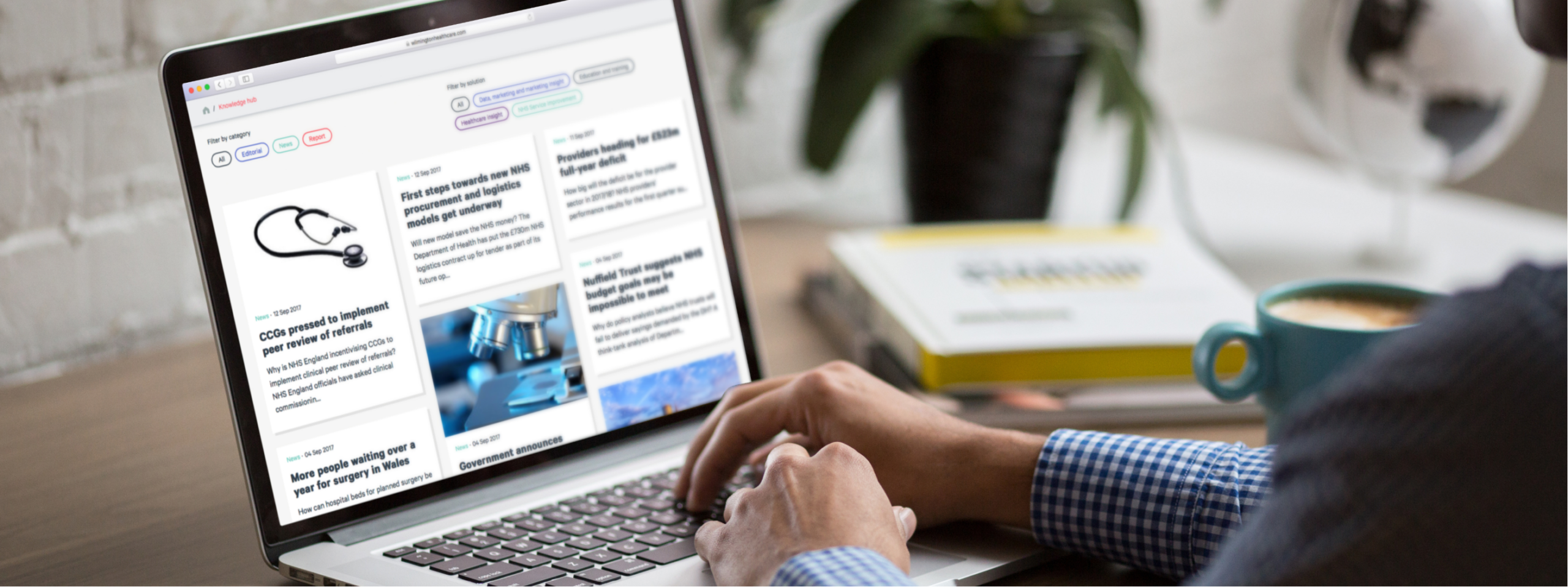 a stock photo of a man in a cafe on a laptop with the wilmington healthcare news page in view in the screen.